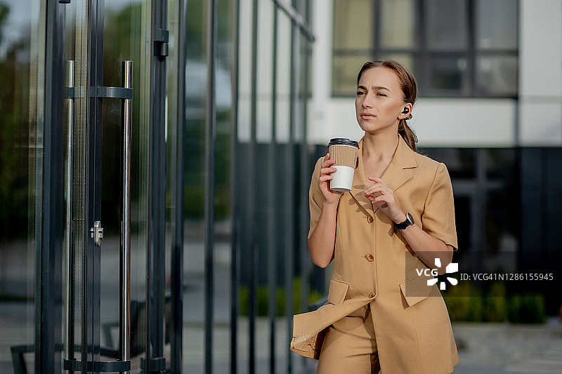 在城市街道上，成功的商业女性律师手里拿着一杯热饮在上班的路上。白人女商人在外面开心地笑着图片素材