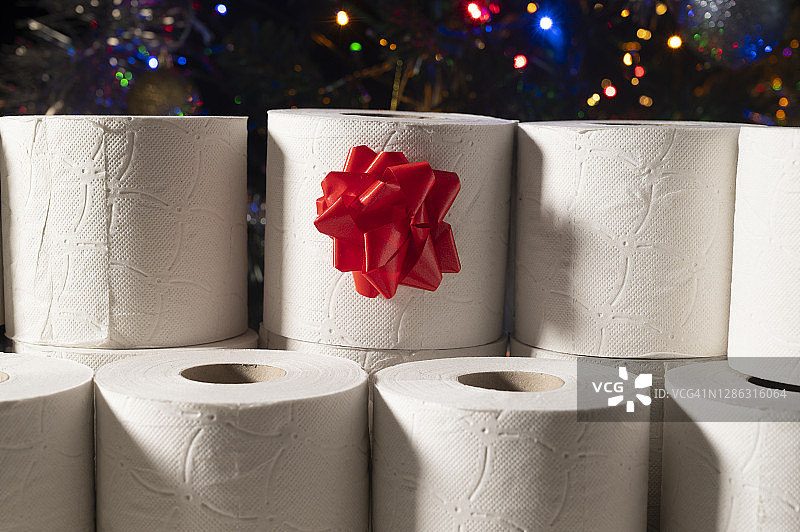 圣诞礼物:卫生纸的角色。在模糊的背景中，有一棵装饰着彩灯的圣诞树。图片素材