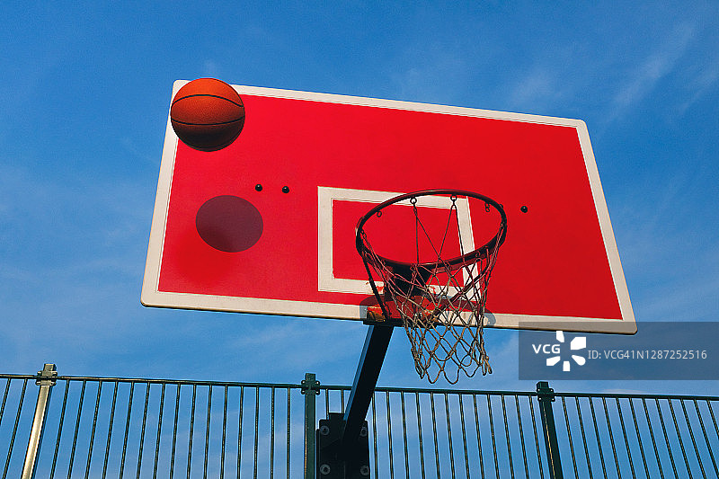 在一个开阔的区域，一个篮球飞进了篮筐，对着蓝天。运动主题，实现目标。图片素材