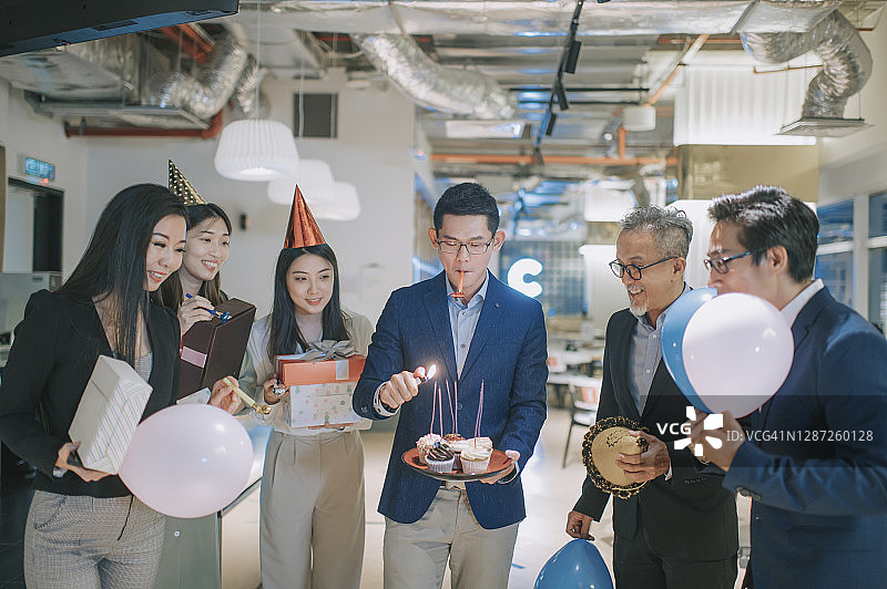 亚洲华人商人点燃生日蜡烛，惊喜办公室生日派对庆祝图片素材