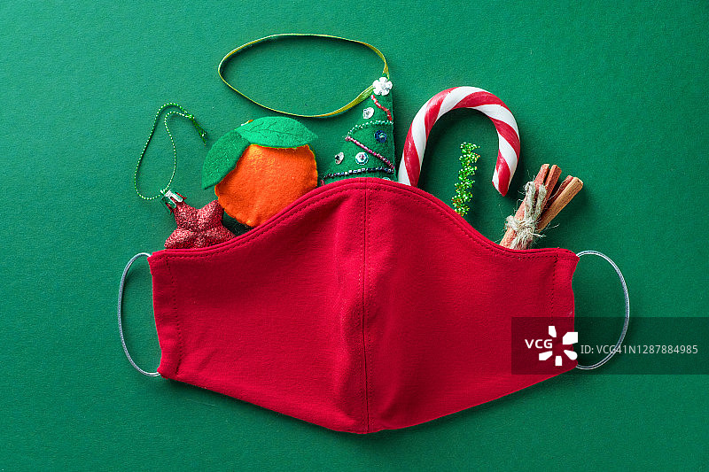 红色医用防护口罩，条纹糖果手杖，手工圣诞树玩具，肉桂，银丝在绿色的背景。预防和预防COVID - 19大流行的传播。快乐健康圣诞的理念。图片素材