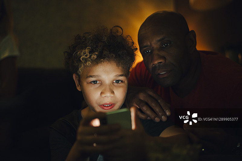 男孩晚上在客厅用爸爸的智能手机图片素材