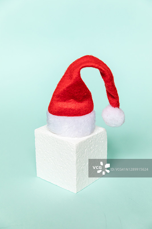 简单的最小组成冬季物体，圣诞老人的帽子和立方体形状，几何形式讲台孤立的蓝色蜡笔背景。12月圣诞新年时间为庆祝概念。空间模型,复制图片素材
