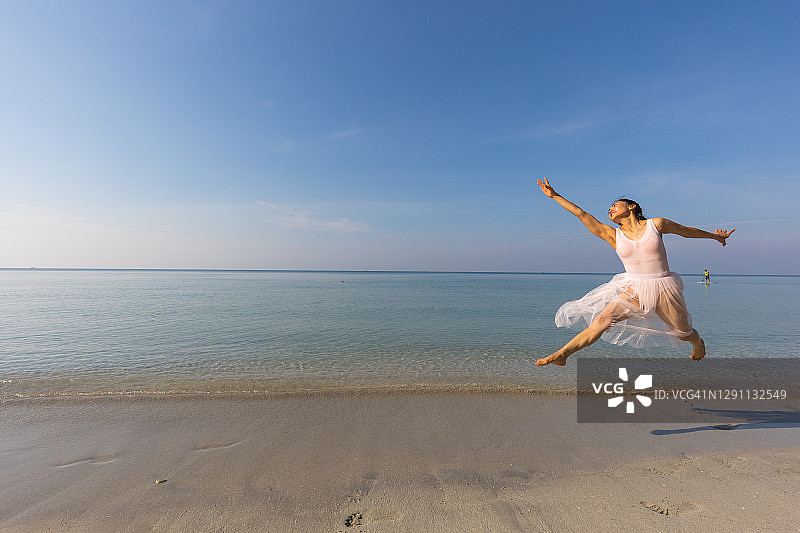 亚洲女人穿着白色的裙子在海滩上跳芭蕾舞。图片素材