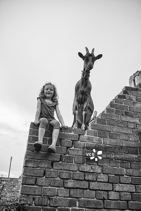 微笑的女孩坐在墙上，旁边是一只山羊，波兰图片素材