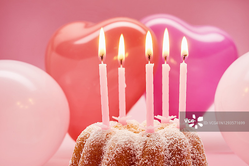 在粉红色的背景下，粉红色蜡烛和气球的心形生日蛋糕的静物图片素材