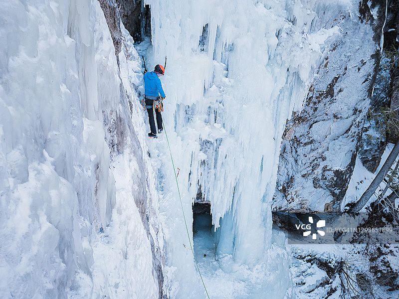 在不列颠哥伦比亚省的内陆，一名男性冰上攀登者正在攀爬一个高高的、垂直的冰冻瀑布图片素材