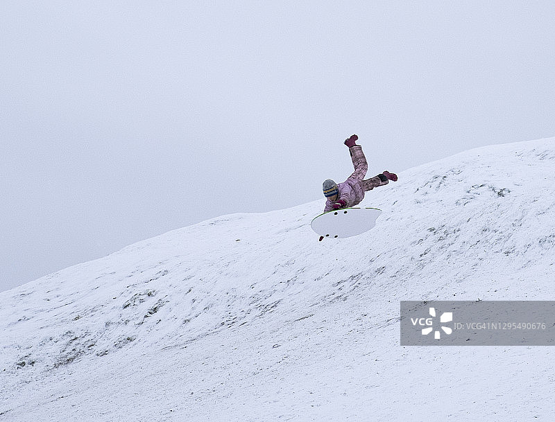 一个孩子，一个男孩，正在飞快地从一座积雪覆盖的山上滑下来。冬天好玩的周末。图片素材
