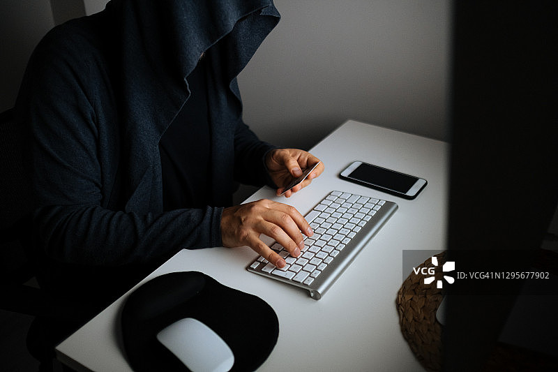 一名穿着连帽衬衫和面具的男子在黑暗中使用笔记本电脑黑客图片素材