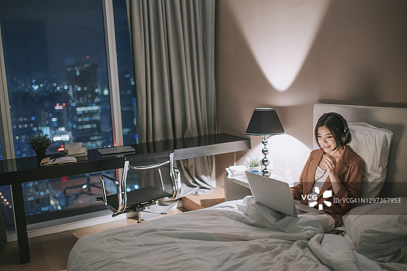 亚洲华裔美女晚上在卧室里用笔记本电脑进行视频通话图片素材