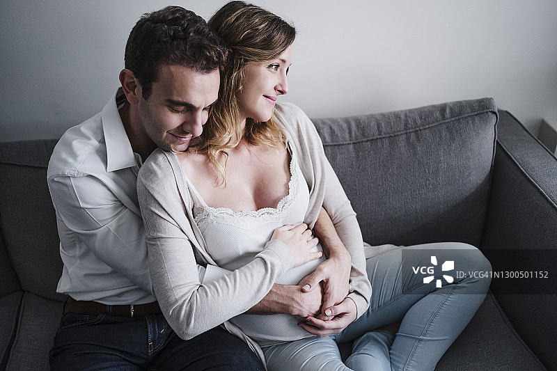坐在家里沙发上，男人闭着眼睛拥抱着怀孕的妻子图片素材