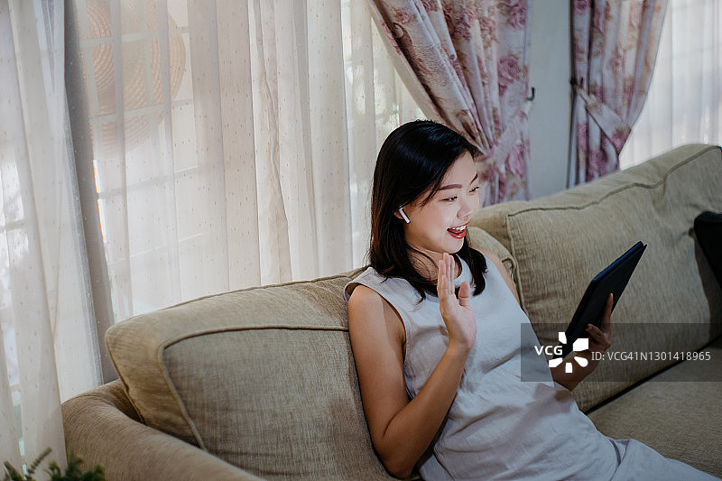 年轻的亚洲女人在客厅用平板电脑打视频电话图片素材