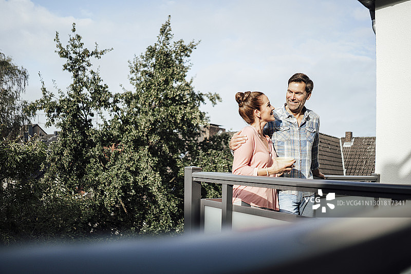 在阳光明媚的日子里，一对成熟的情侣站在阳台上，看着对方微笑着图片素材