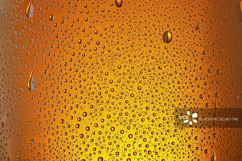 饮用玻璃-玻璃瓶上的凝结。冰啤酒杯与水滴橙色背景图片素材