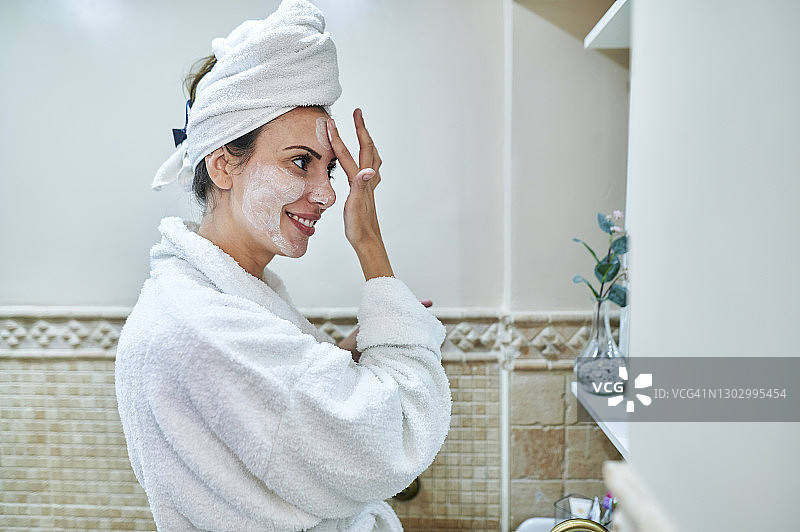 微笑的女人站在浴室里涂面霜图片素材