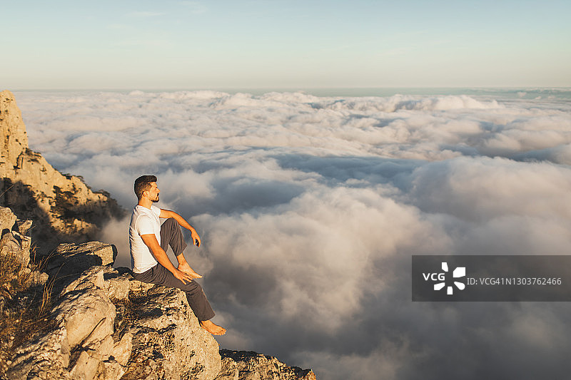坐在山崖边的人，欣赏着天上的景色。令人惊叹的低云景观图片素材
