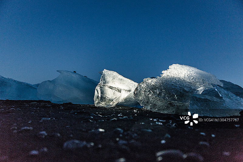 黄昏时分，黑色沙滩上的小冰山上有一个被照亮了。图片素材