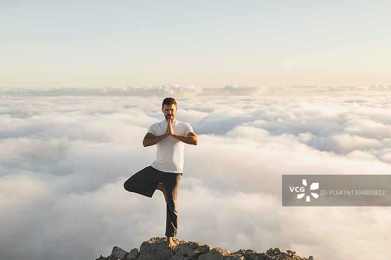在早晨，一个人在山上独自练习哈他瑜伽(树式)，看到令人惊叹的低云图片素材