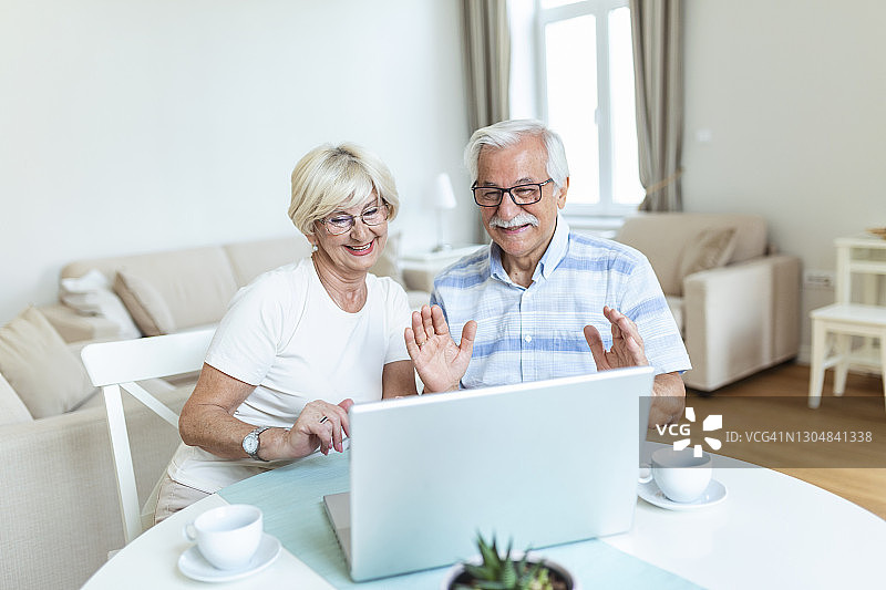 幸福的老夫妇和家人朋友聊天用笔记本电脑，惊讶兴奋的女子看着电脑挥手微笑。图片素材