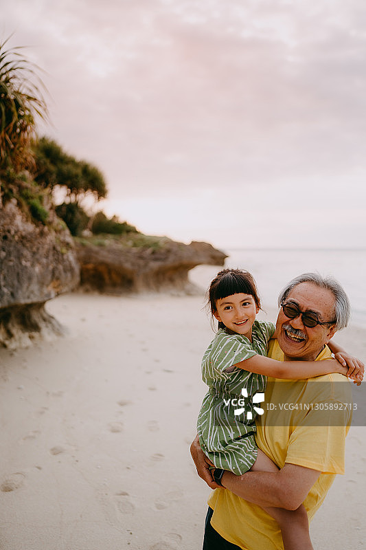 日落时分，快乐的爷爷在海滩上拥抱孙女图片素材