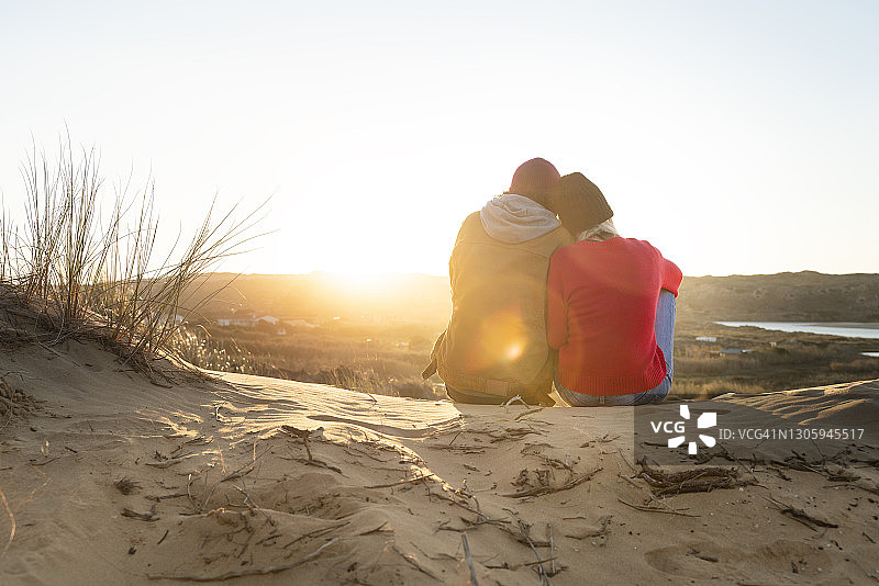 日落时分，坐在沙丘上的女人靠在男人的肩膀上图片素材