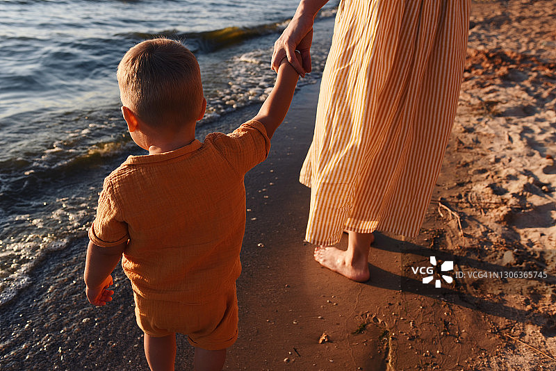 妈妈牵着孩子的手沿着海滩走。图片素材