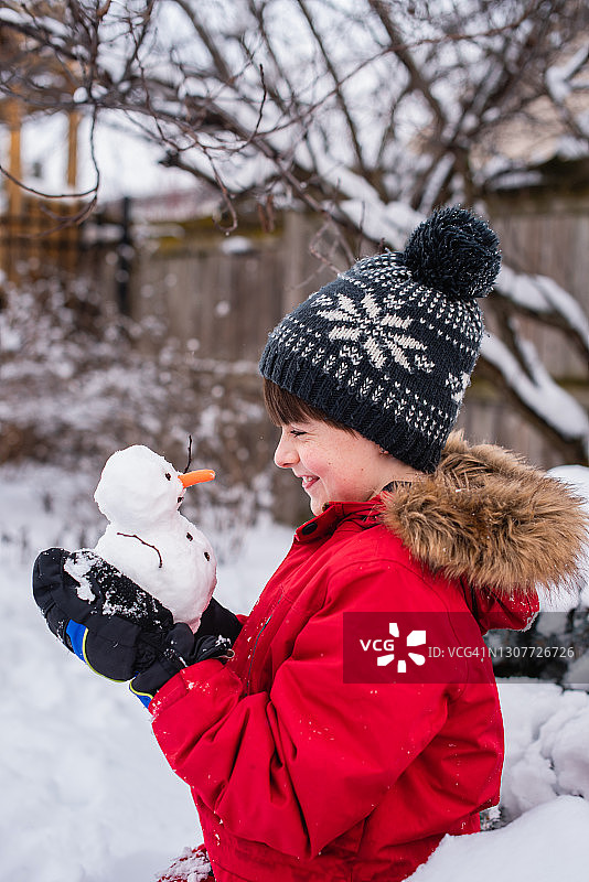 在一个下雪天，一个男孩在户外抱着一个小雪人。图片素材