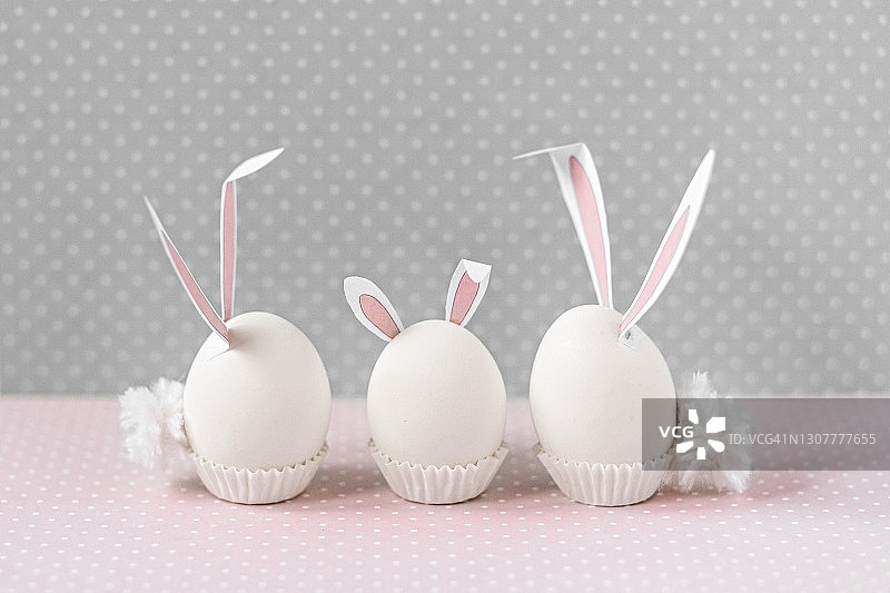 白色的鸡蛋，兔子耳朵和尾巴在床上花的背景。一个家庭。复活节节日快乐概念图片素材