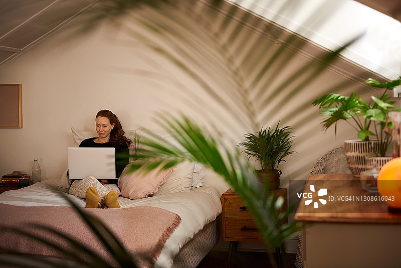 年轻女子在家里的床上用笔记本电脑工作图片素材