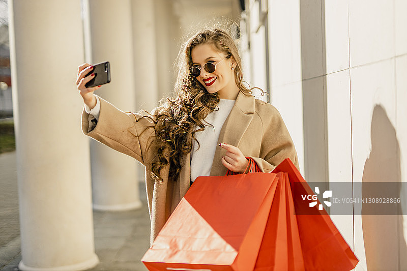 一张年轻女子在城市购物的照片，同时用她的手机自拍和微笑图片素材
