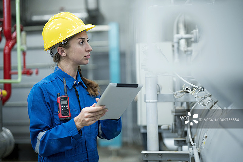 智能女维护工程师在工厂锅炉控制室使用数字平板站在泵阀控制面板前检查蒸汽锅炉的压力和温度以及测量记录。图片素材