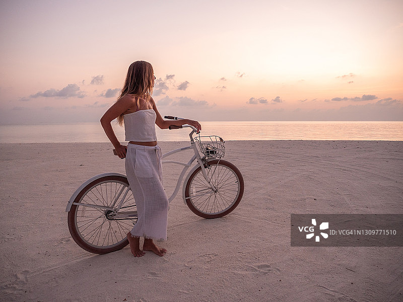 日落时分，年轻女子骑着自行车在海滩上图片素材