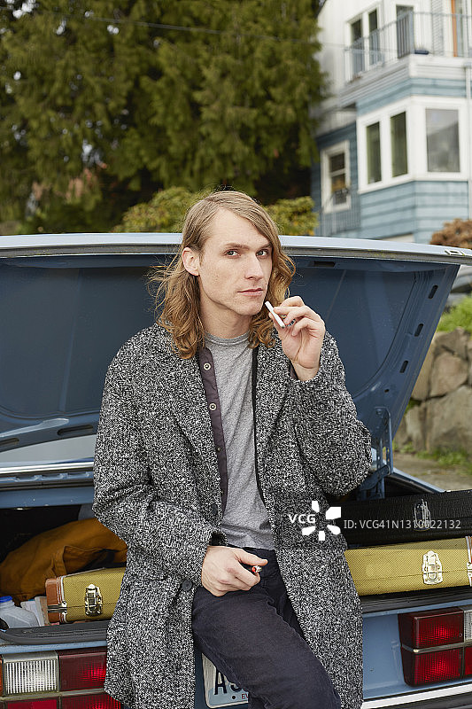 年轻男子站在汽车后备箱边抽烟图片素材