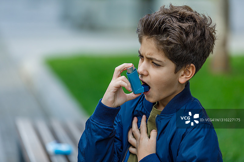 哮喘小男孩在公园里使用吸入器。图片素材