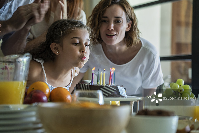 小女孩吹蜡烛的生日蛋糕，她的家人唱歌的背景图片素材