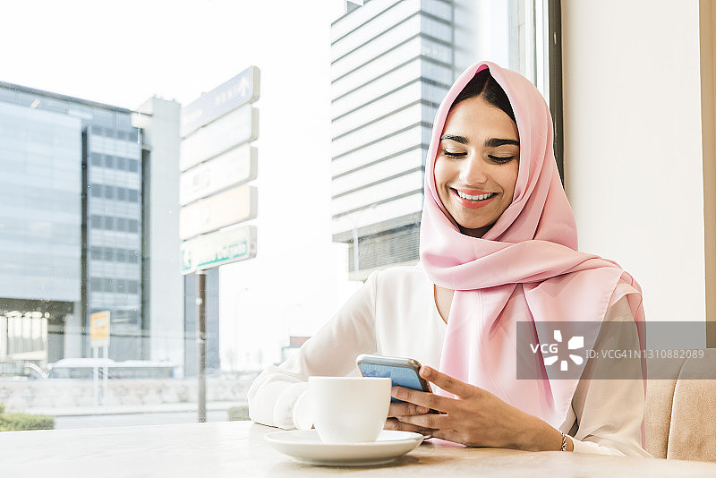 一名年轻的阿拉伯女子坐在咖啡店里查看她的社交网络图片素材