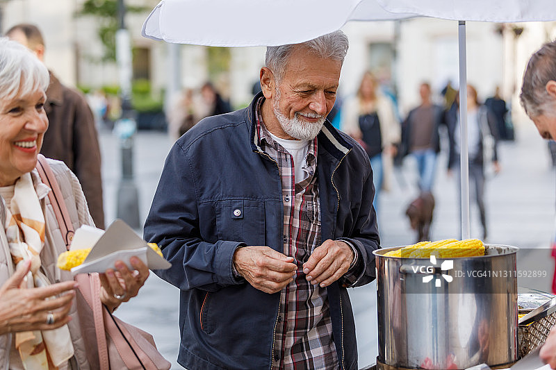 一个老人和他的妻子在城市散步吃玉米的肖像。图片素材