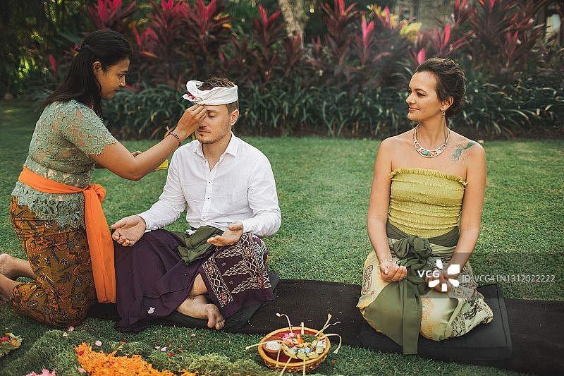巴厘岛女子身着传统服饰，为欧洲白种夫妇举行神圣的婚礼图片素材