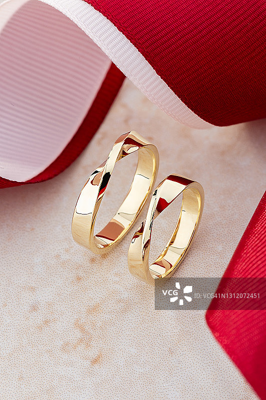 高角度视图对时尚的金结婚戒指米色背景与红色丝带图片素材
