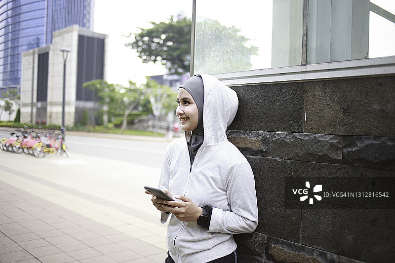 年轻的亚洲女性戴着头巾，用手机，穿着运动服图片素材