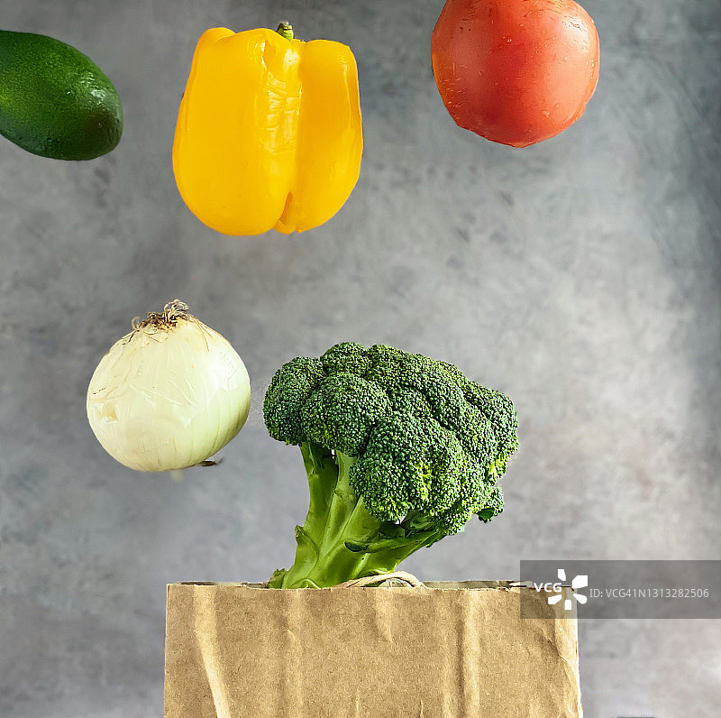 蔬菜西红柿，甜椒，洋葱，花椰菜悬浮在购物纸袋上。健康的生活方式和营养观念。图片素材