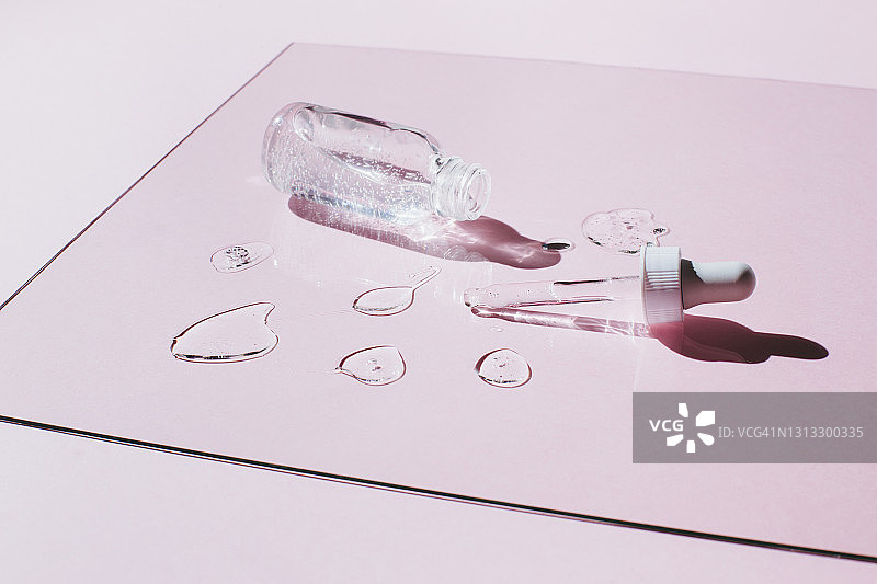 液体凝胶和血清滴液与玻璃瓶附近的移液管在粉红色的背景。美容产品与肽，神经酰胺，透明质凝胶。图片素材