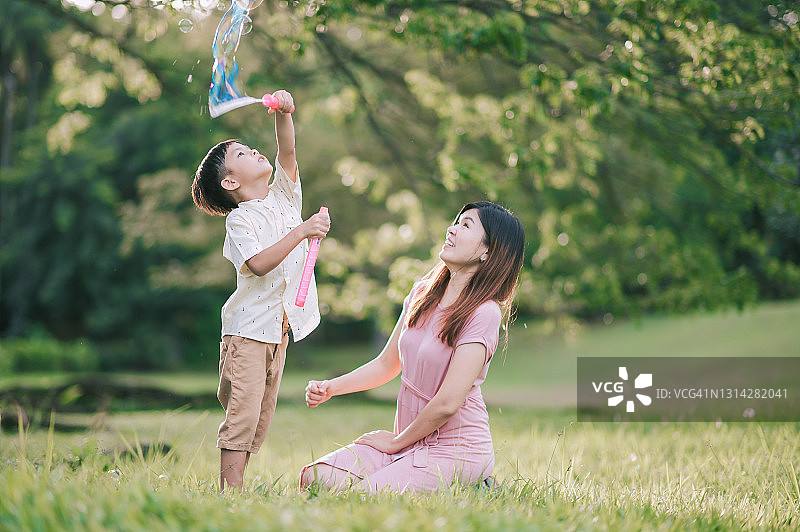 亚洲华人母亲和她的儿子在公园玩泡泡棒在早晨背光的阳光图片素材