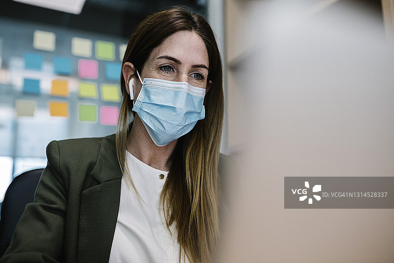 2019冠状病毒病期间戴防护口罩在办公室工作的女性企业家图片素材