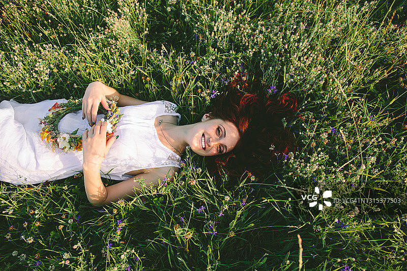 一个年轻的红发女子戴着春天的花环躺在草地上，休息着，微笑着，思考着，享受着夏日的温暖和她的生活图片素材