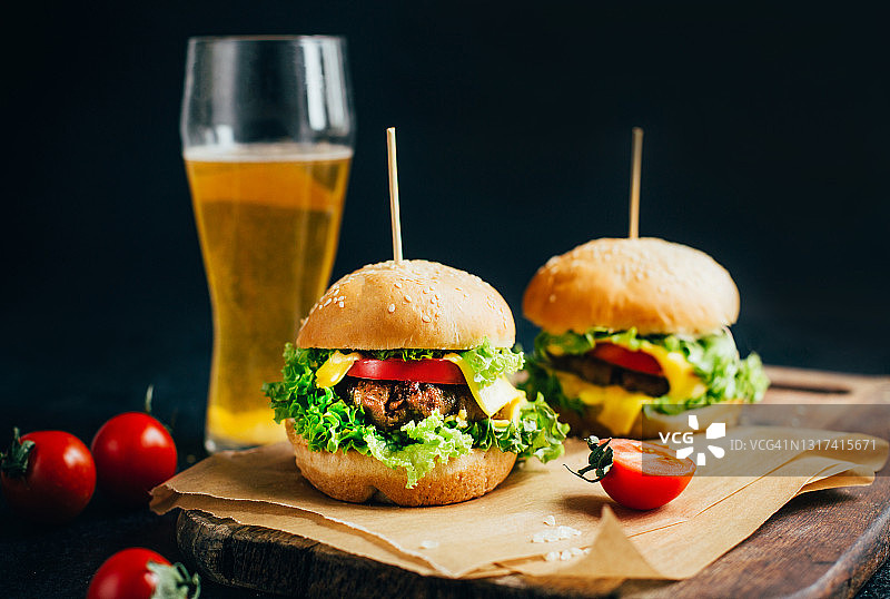 一个汉堡包与肉在烧烤，西红柿和绿色的背景上的一个玻璃与啤酒在一个黑色的背景图片素材