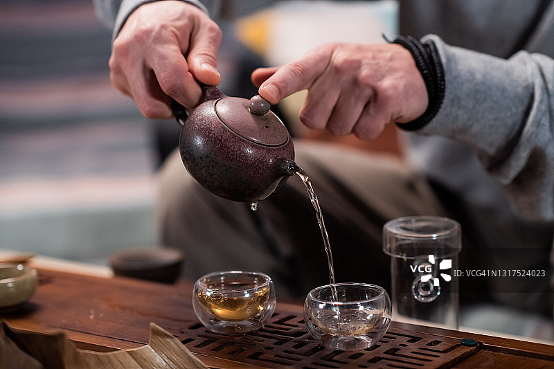 镜头拉近了茶馆里一位茶艺大师的手，他在竹制的桌子上用一个托盘将茶倒在特制的杯子里供品尝图片素材
