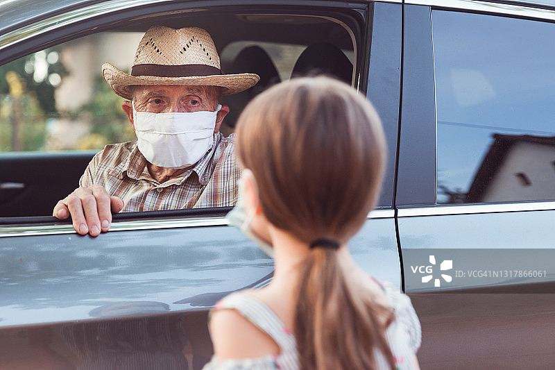 老人戴着防护面具坐在车里和站在车外的孙女聊天图片素材