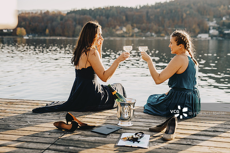 女性活动策划者坐在湖边的防波堤上举杯庆祝图片素材