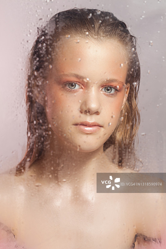 年轻美丽的女人有着完美的皮肤在玻璃后面有雨滴在粉红色的背景图片素材